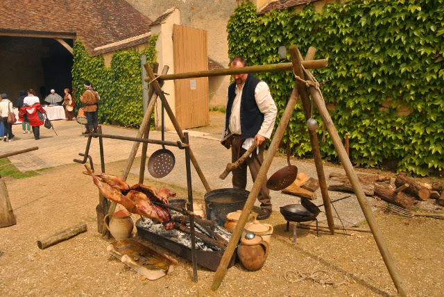 Des coquemars devant les braises et l'agneau embroché au dessus de la lèche-frite